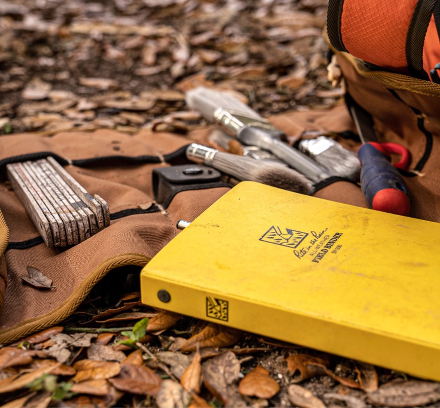 Rite in the Rain Binder laying along side archeaologist tools and bag.