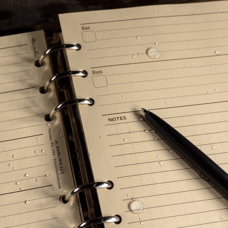 Open planner with pen resting on wet planner loose leaf.
